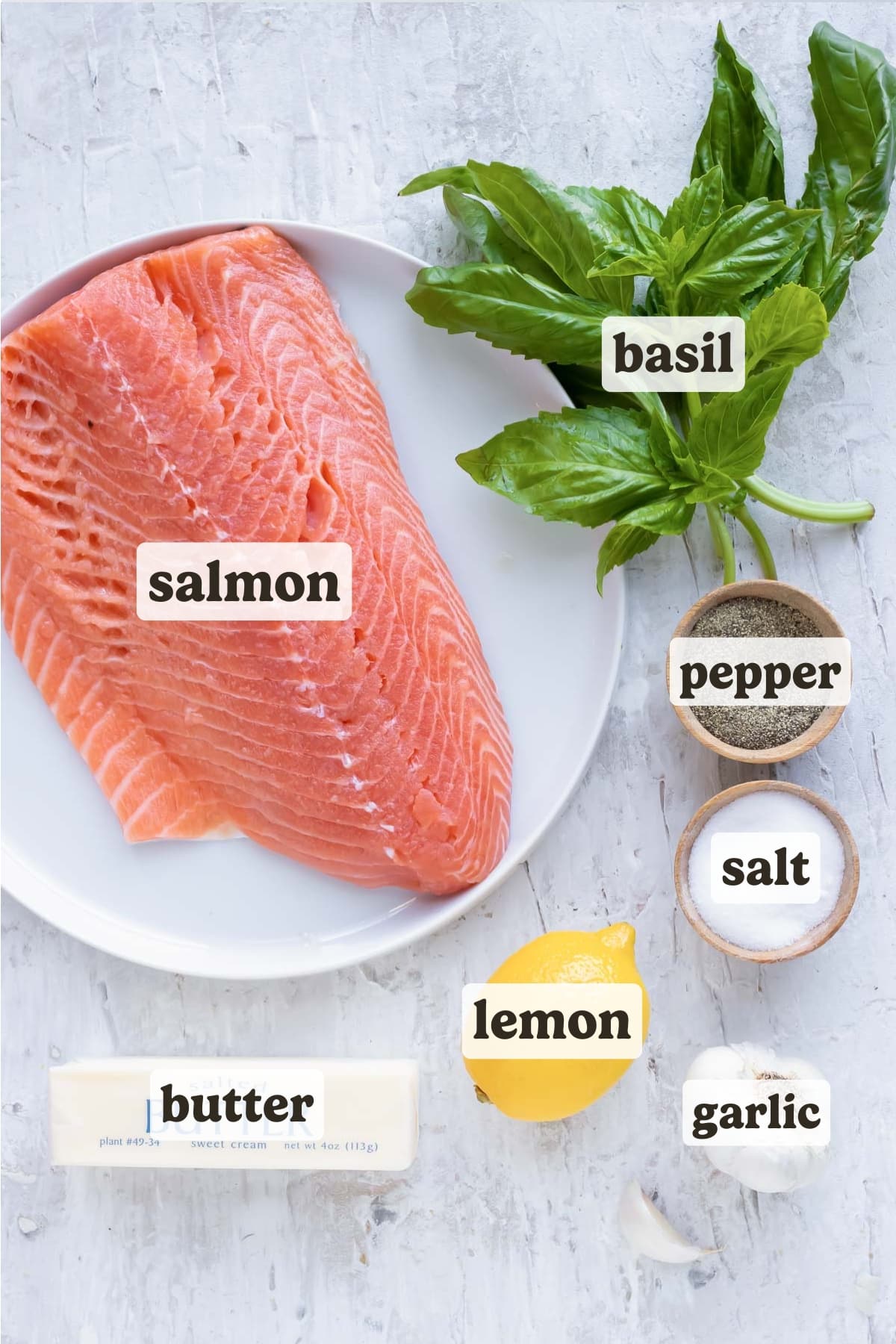 A pound of salmon, fresh basil, a lemon, garlic, salt, pepper, and butter - showing ingredients.