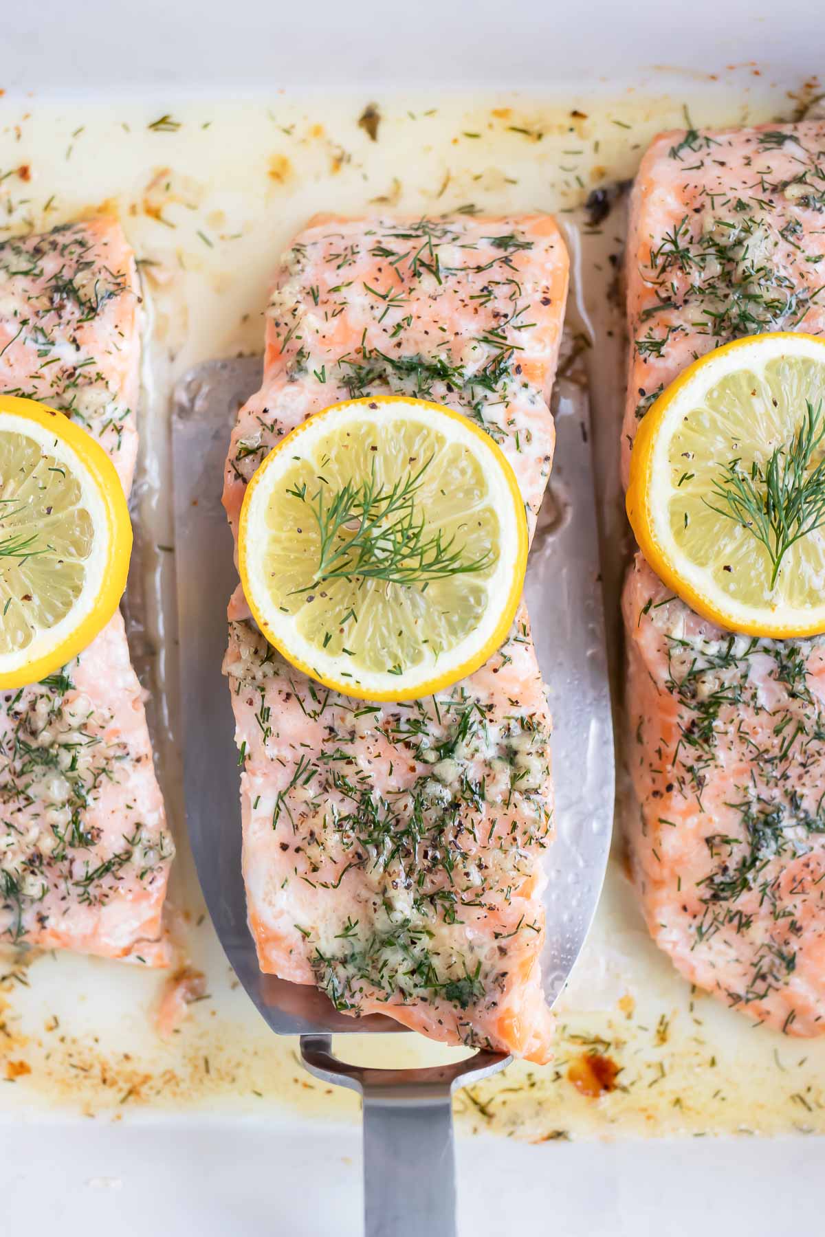 A piece of lemon dill salmon is lifted up by a spatula.