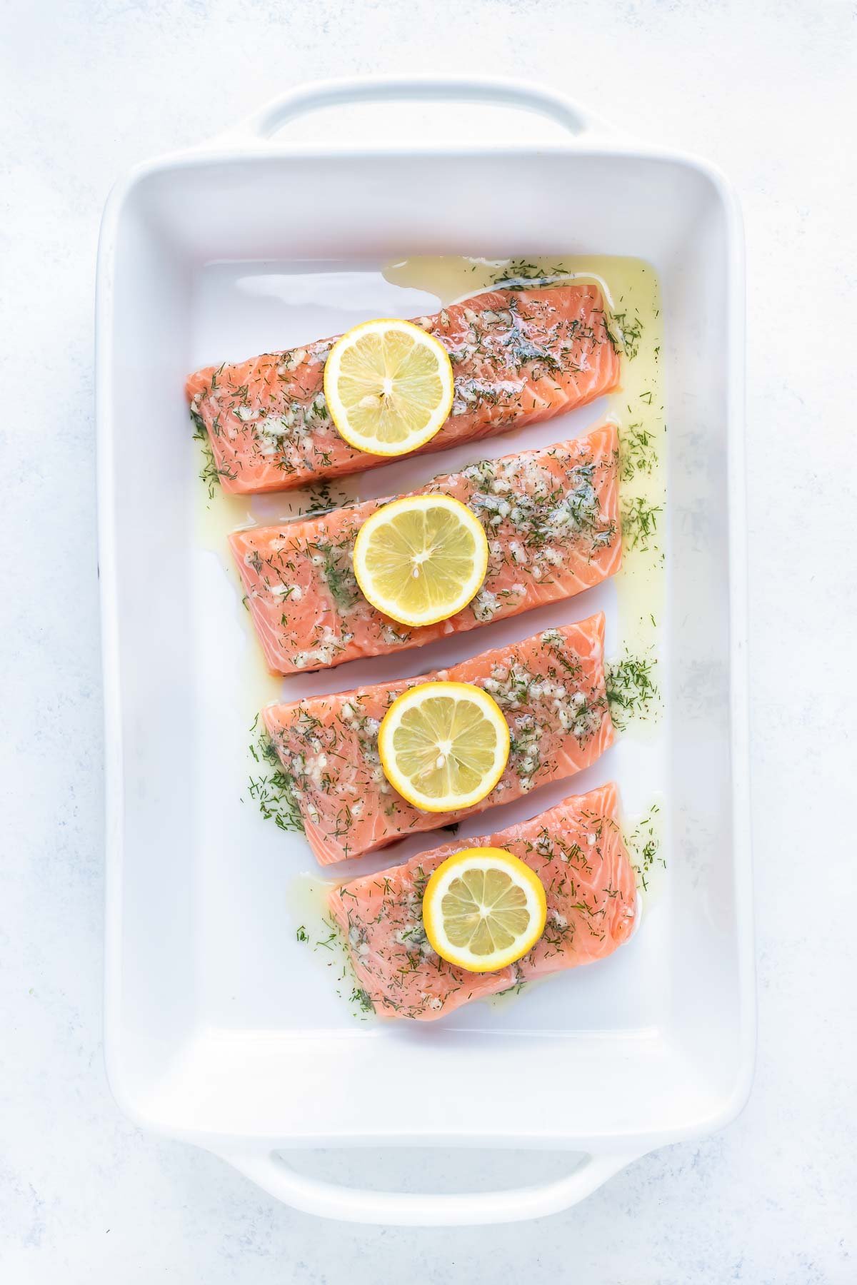 Salmon is topped with a garlic butter sauce with lemon and dill before baking in the oven.