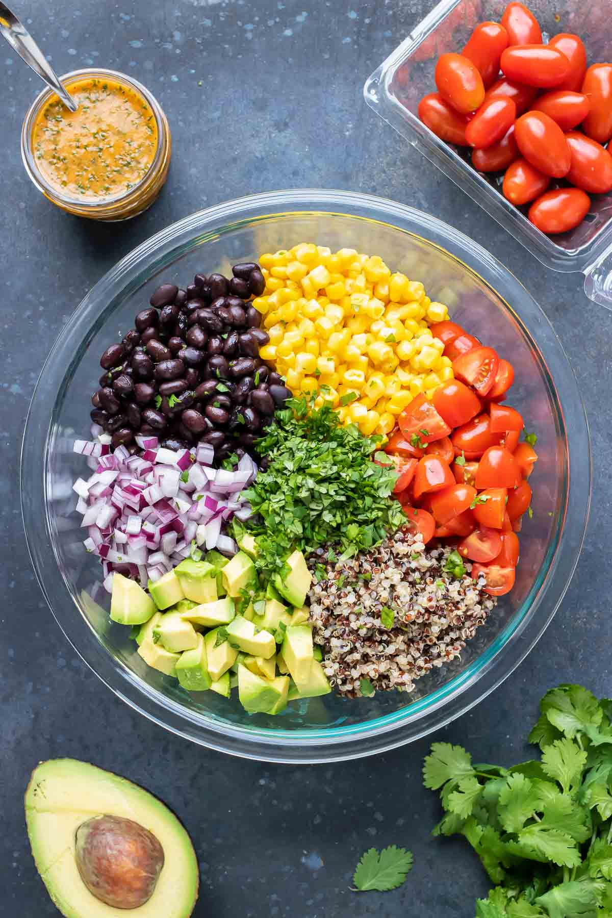 A glass bowl full of black beans, corn, tomatoes, quinoa, avocado, and red onions.