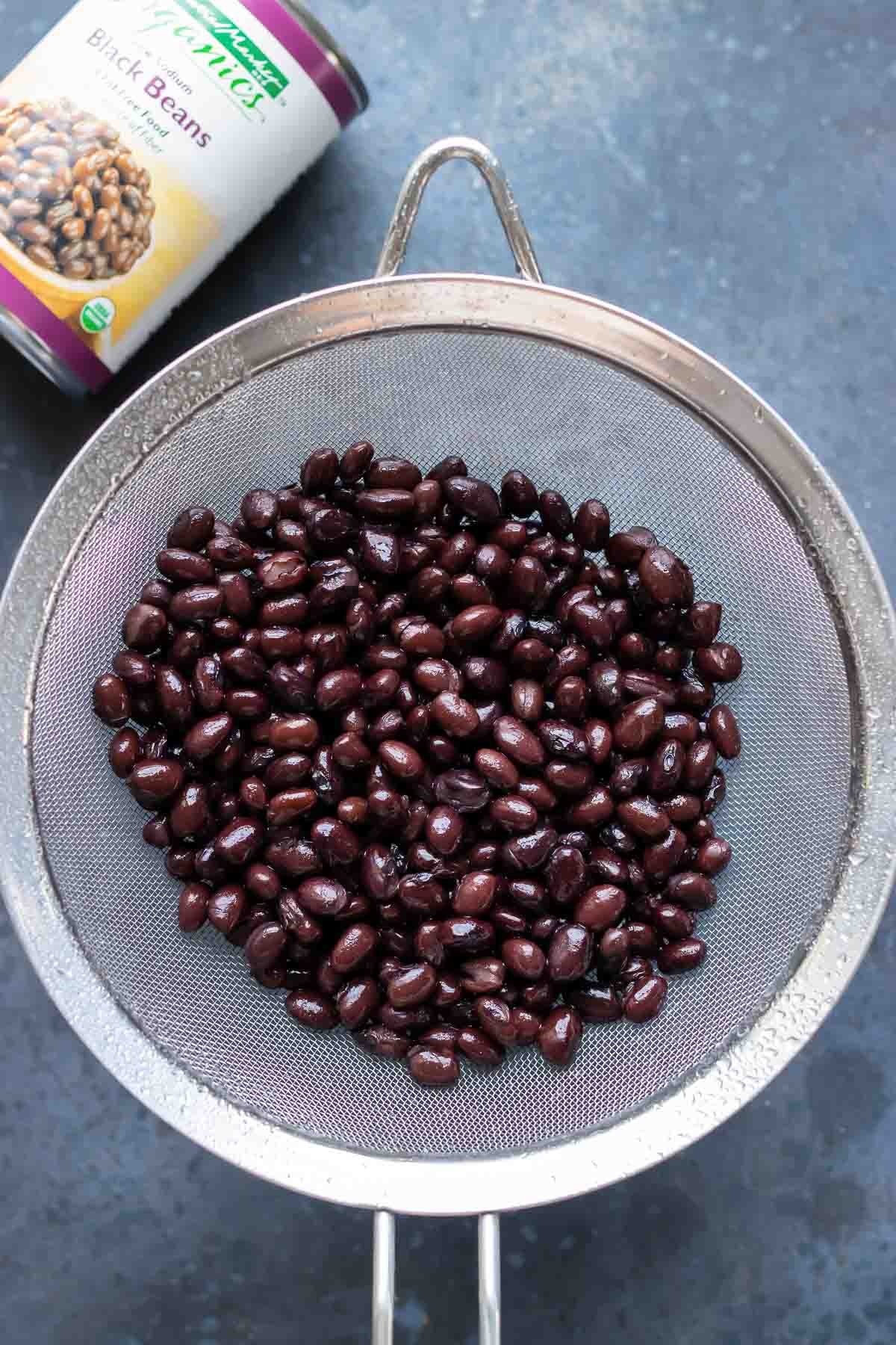 Black beans draining in a metal strainer with the original can in the background.