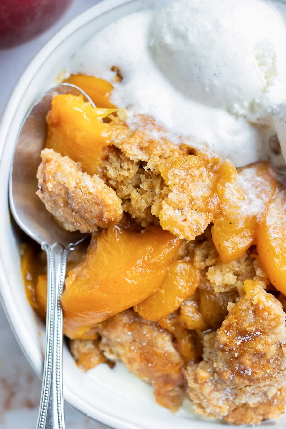 The best peach cobbler recipe is in a white bowl and served with vanilla ice cream.