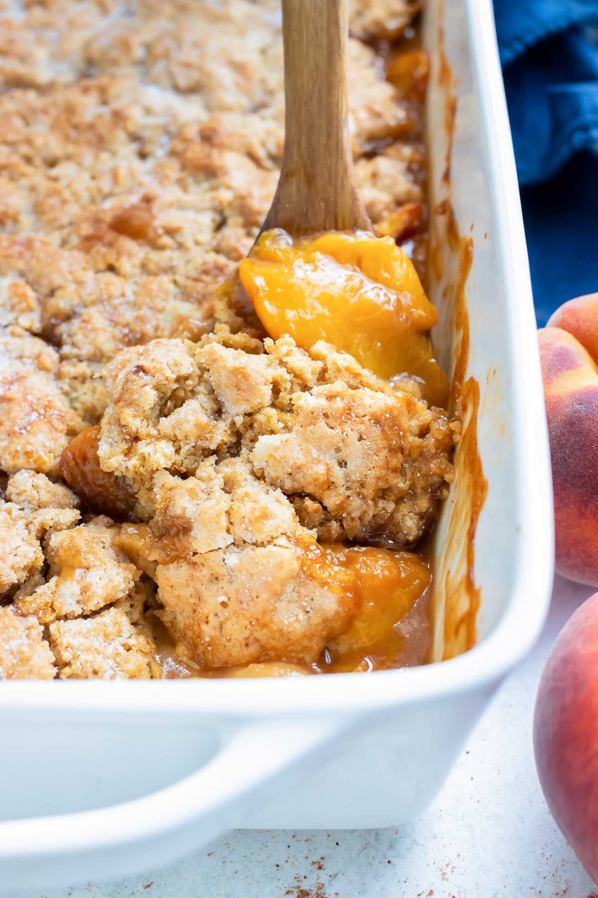 Tender peaches and a buttery topping are being served out of a baking dish for a southern peach cobbler dessert.