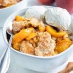 A big bowl of healthy, homemade cobbler made with tender peaches is topped with two scoops of vanilla ice-cream.