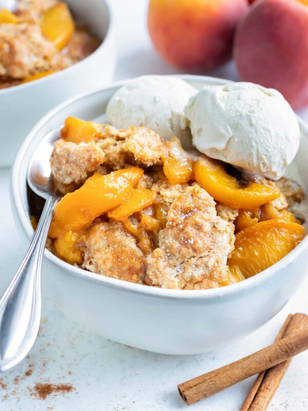 A big bowl of healthy, homemade cobbler made with tender peaches is topped with two scoops of vanilla ice-cream.