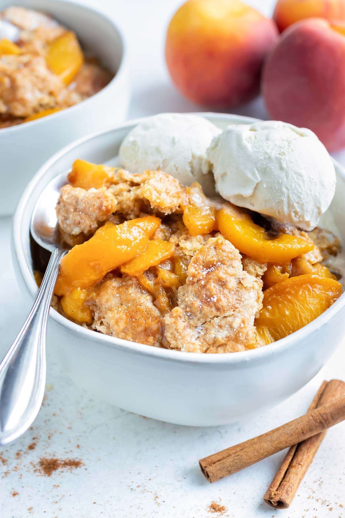 A big bowl of healthy, homemade cobbler made with tender peaches is topped with two scoops of vanilla ice-cream.
