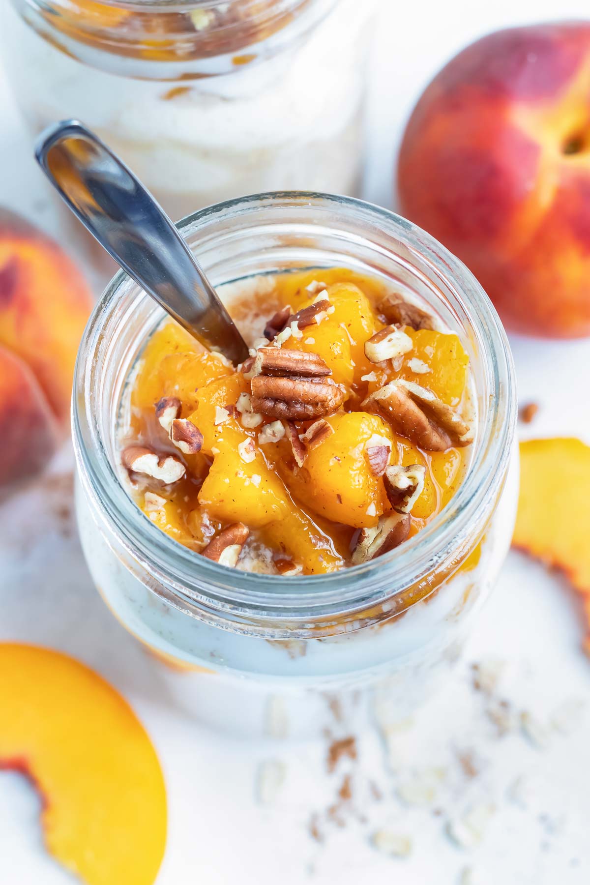 Mason jar peach cobbler overnight oats are topped with fresh peaches and toasted pecans.