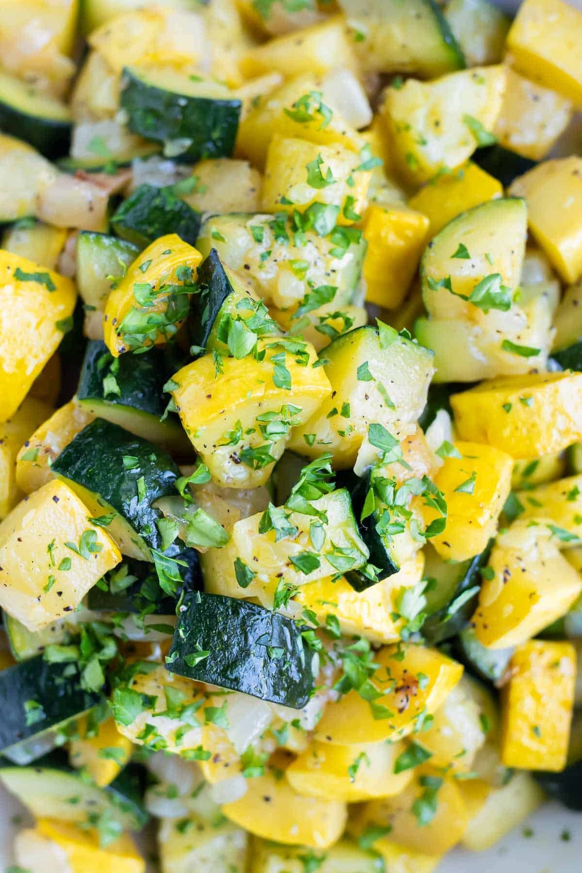 Yellow squash cubes and diced zucchini that have been cooked and sprinkled with parsley.