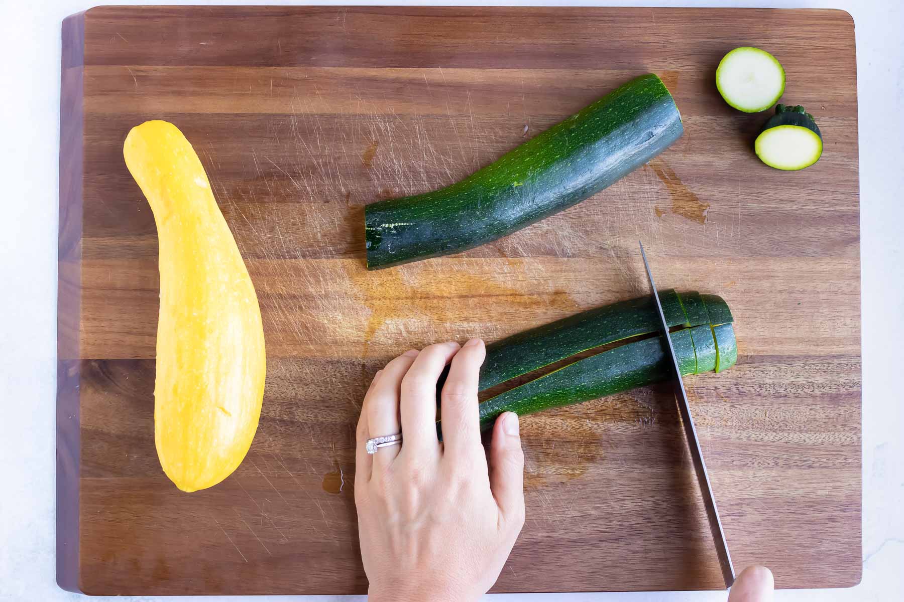 Zucchini and squash are sliced with a sharp knife on a cutting board.