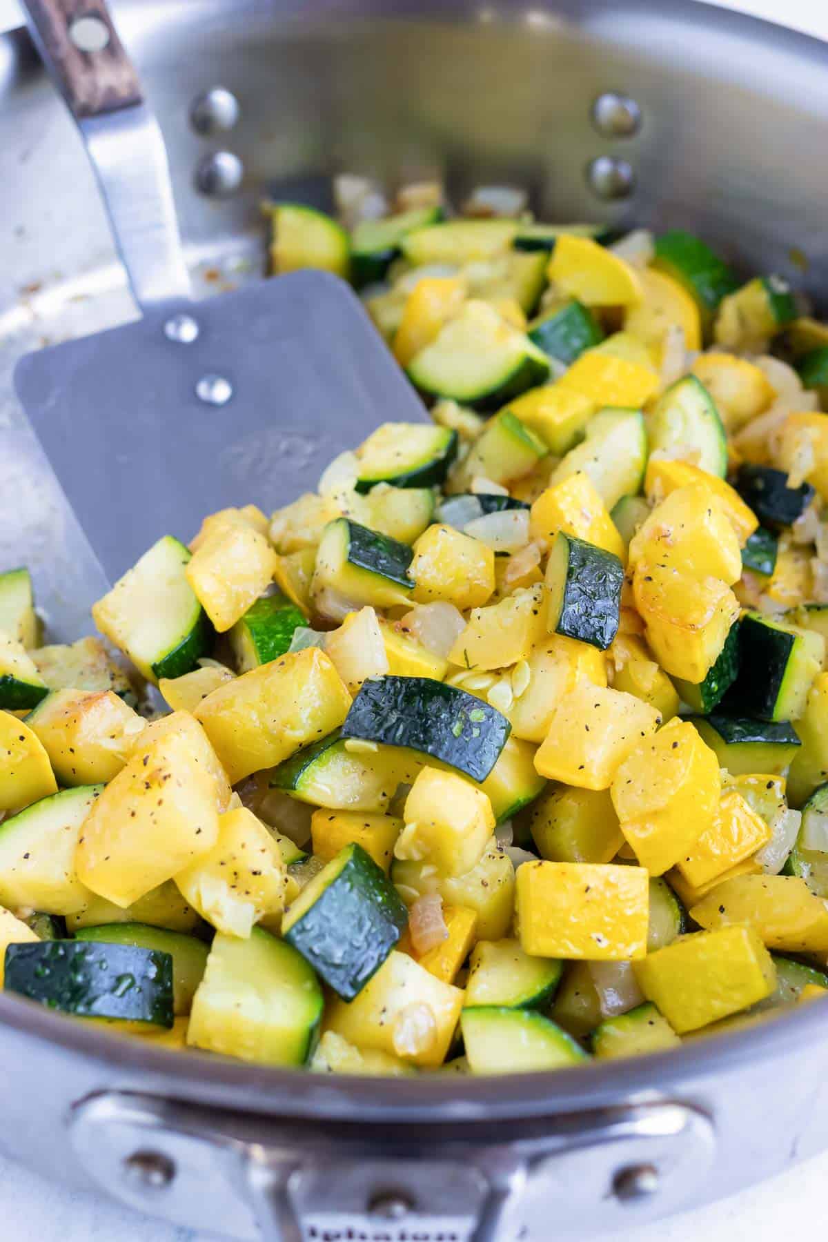 A spatula scooping out a serving of cooked yellow squash and zucchini from a pan.