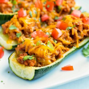 A zucchini squash that has been made into a boat and stuffed with ground beef and taco filling.
