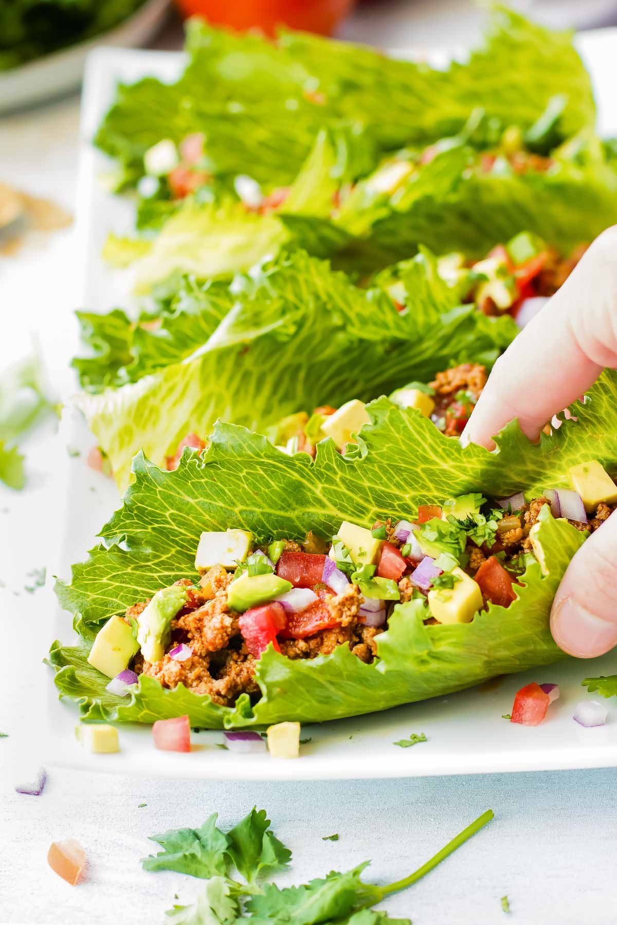 A hand picking up turkey taco lettuce wraps on a white plate.