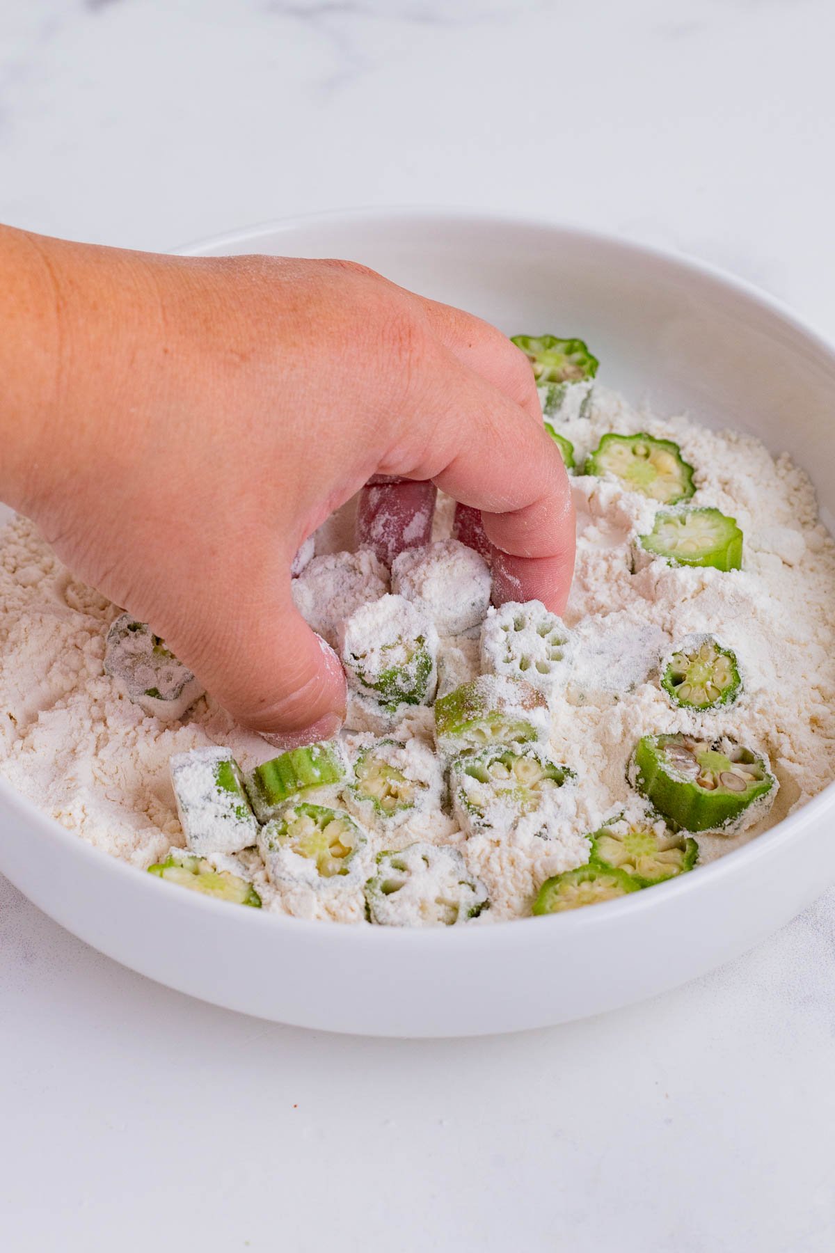 A hand adds okra slices to flour.