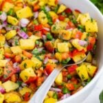 A spoon is used to serve peach salsa from a white, glass bowl.