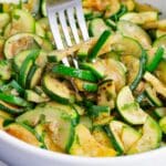A fork digs into the bowl full of sauteed zucchini.