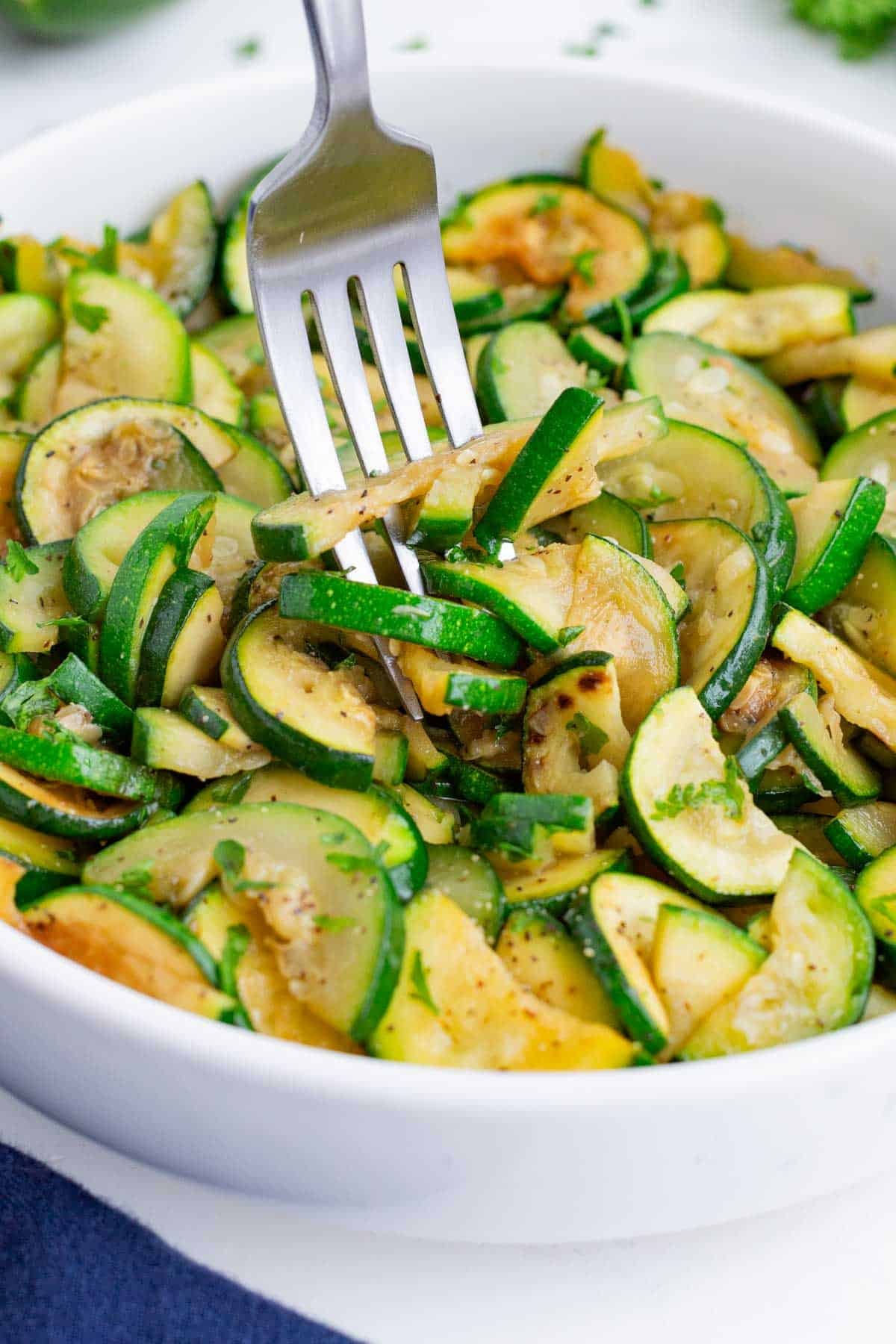 A fork digs into the bowl full of sauteed zucchini.