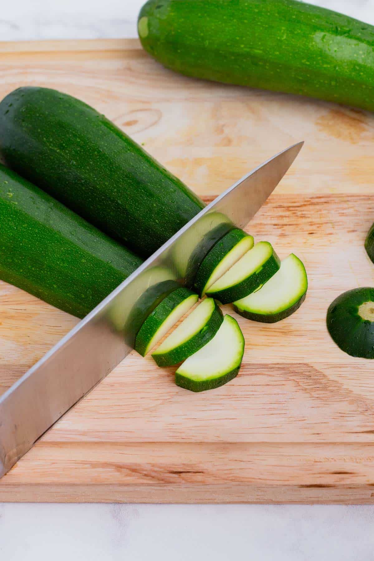 Zucchini being cut in half slices with a knife.