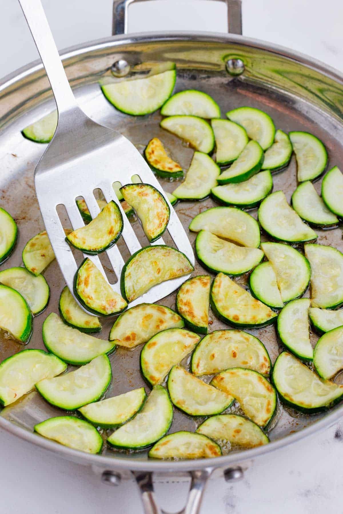 A spatula flips zucchini during cooking.