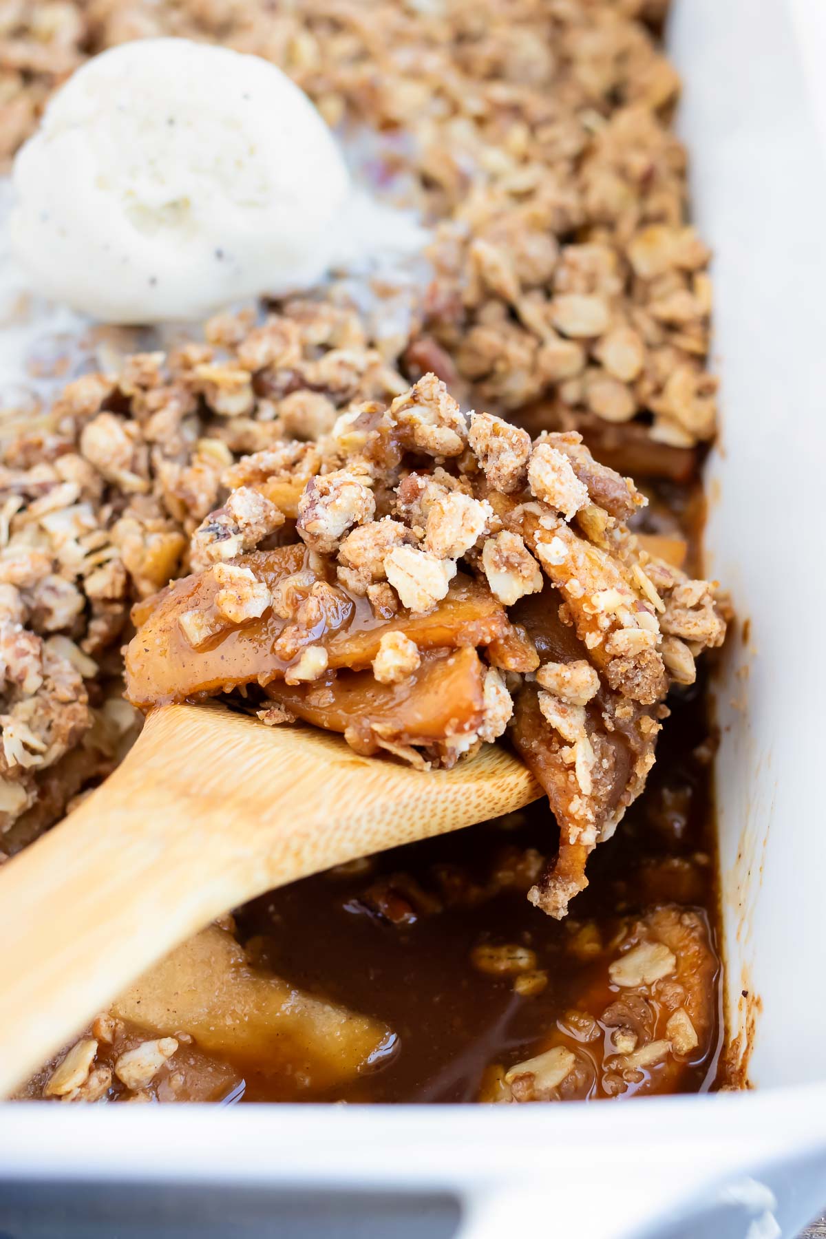A wooden spoon scooping out a serving of a vegan apple crisp.