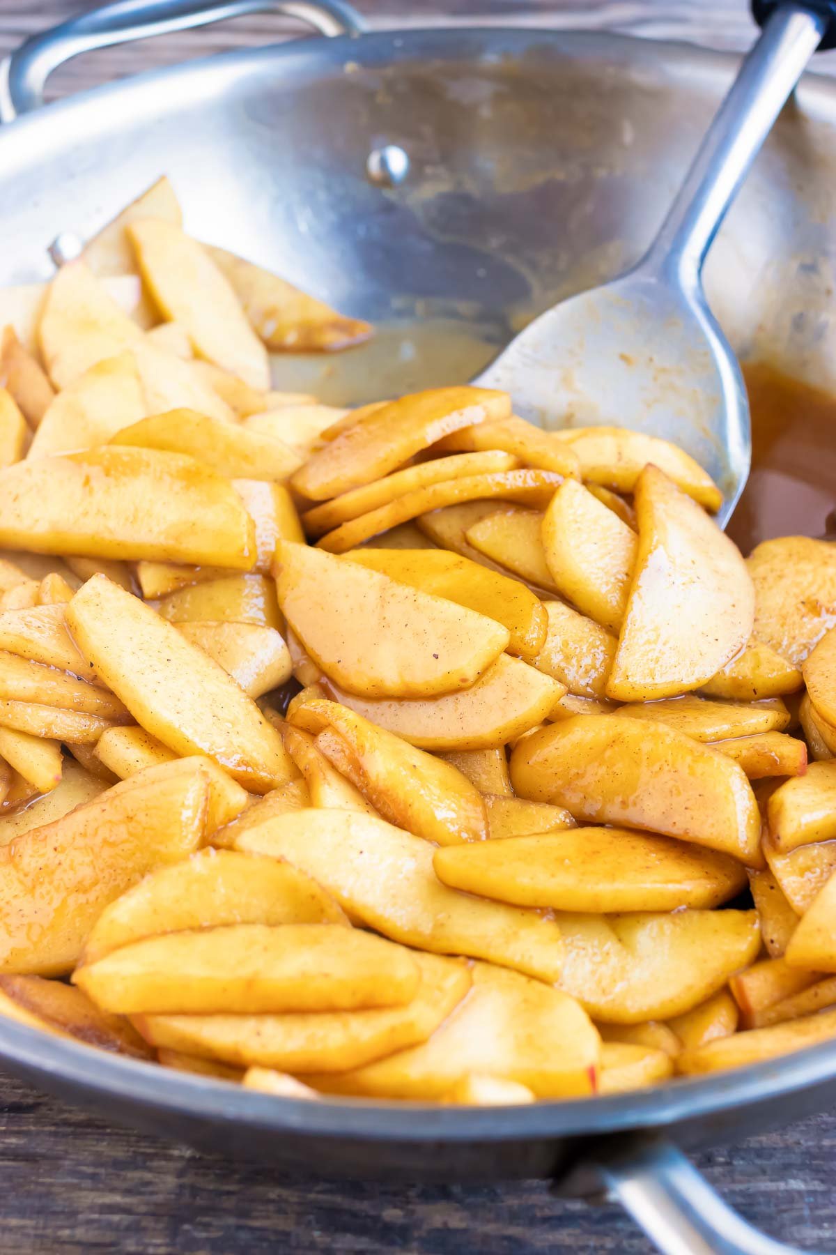 A spoon stirs seasoned apple slices.