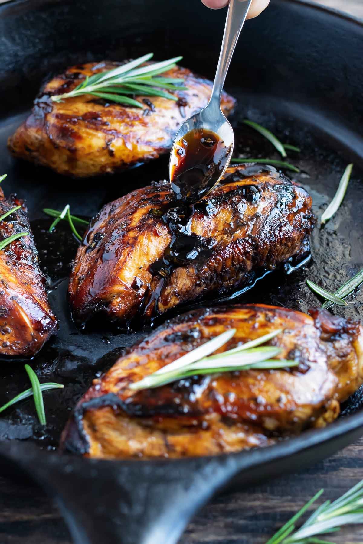 Balsamic glazed being poured over chicken breasts in a cast-iron skillet.