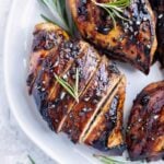 A honey balsamic chicken breast on a white plate with a sprig or rosemary.