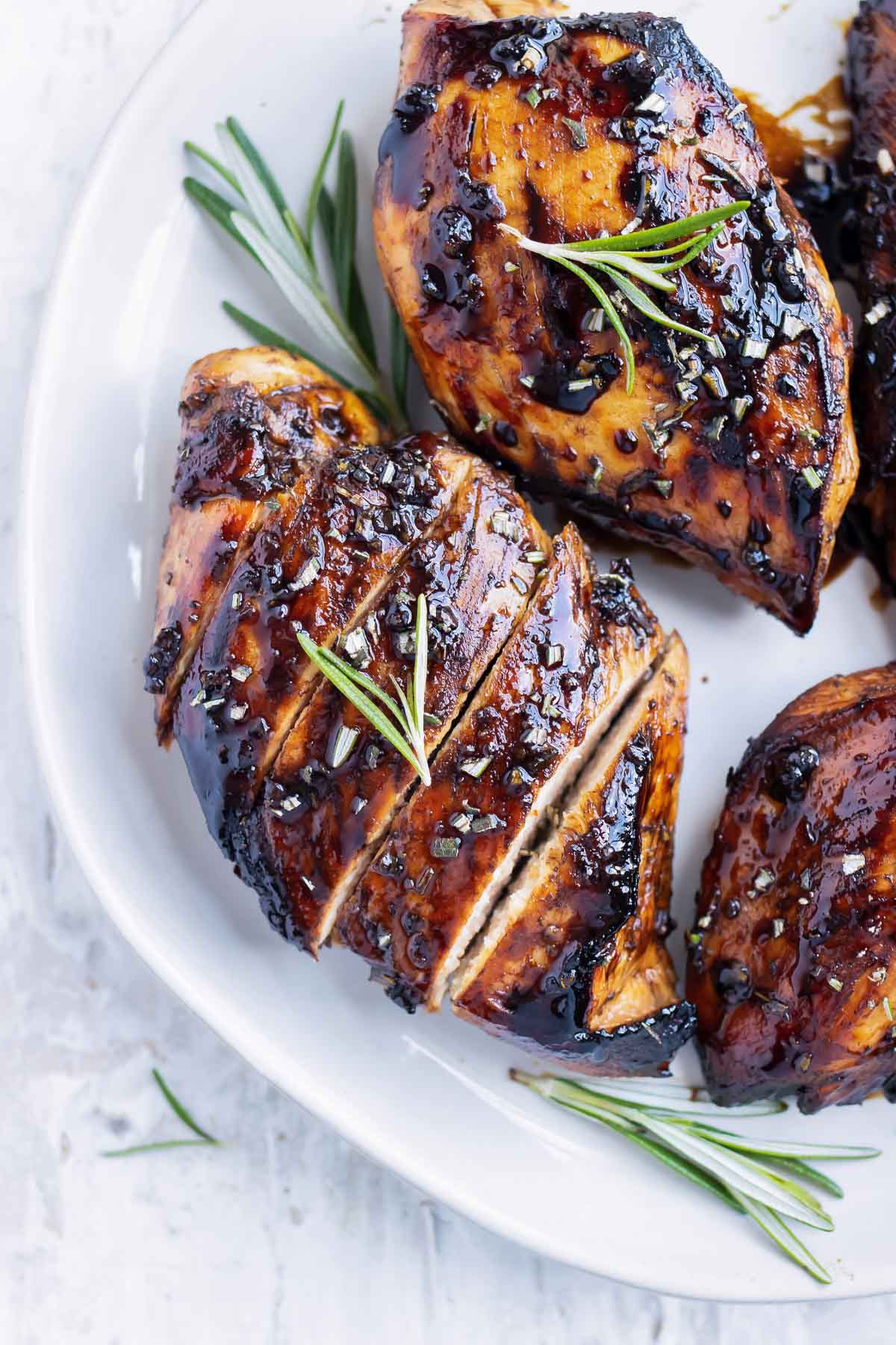 A honey balsamic chicken breast on a white plate with a sprig or rosemary.