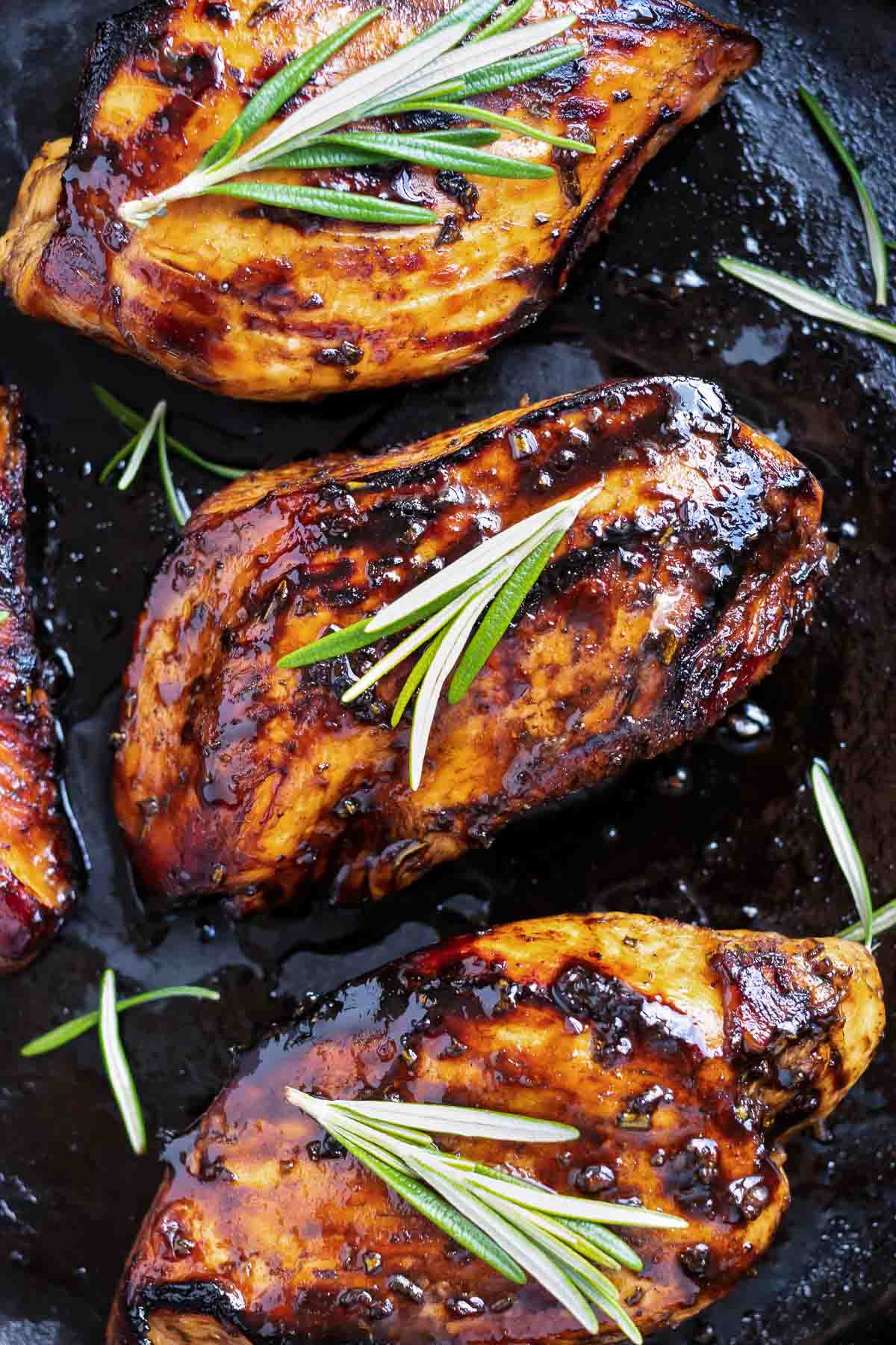 Three balsamic chicken breasts in a row in a black skillet for a healthy dinner recipe.