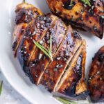 Three balsamic chicken breasts on a white plate with a sprig or rosemary.