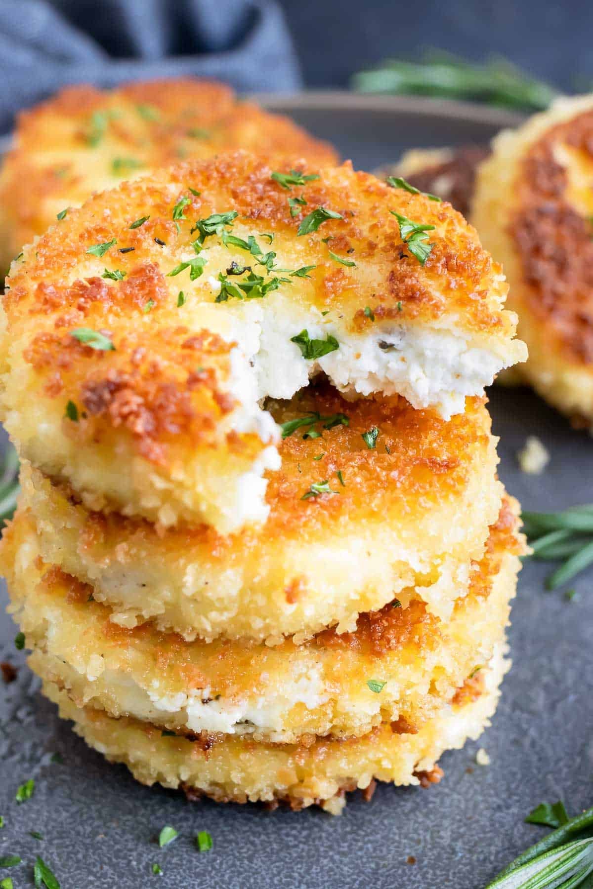 A stack of fried goat cheese slices with a bite taken out of one.