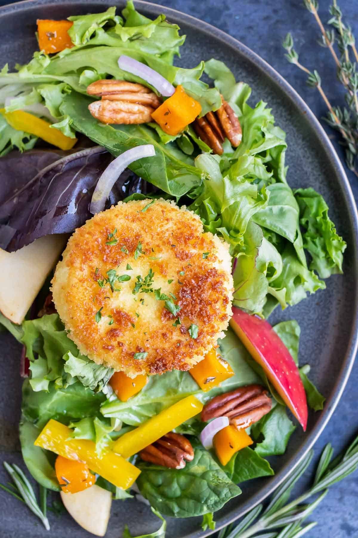 A Fall harvest salad with apples and a fried goat cheese ball on top.