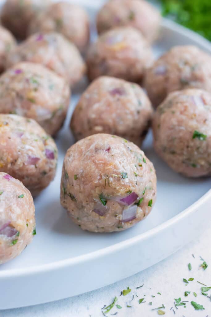 Perfectly formed ground turkey meatballs are placed on a plate before being rolled in gluten-free flour.