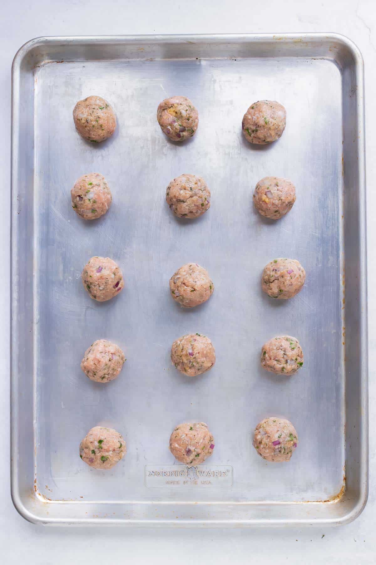 The turkey meatballs are spaced apart on a large baking sheet before being cooked in the oven.