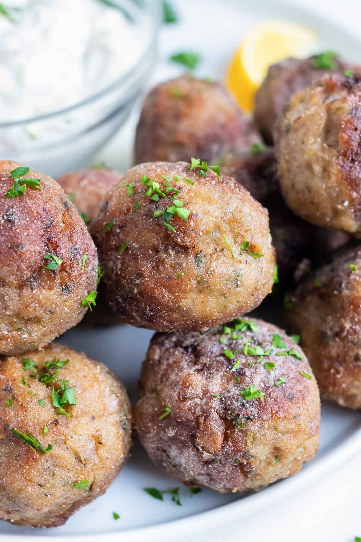 Greek meatballs are served on a plate with fresh lemon and a dipping sauce.