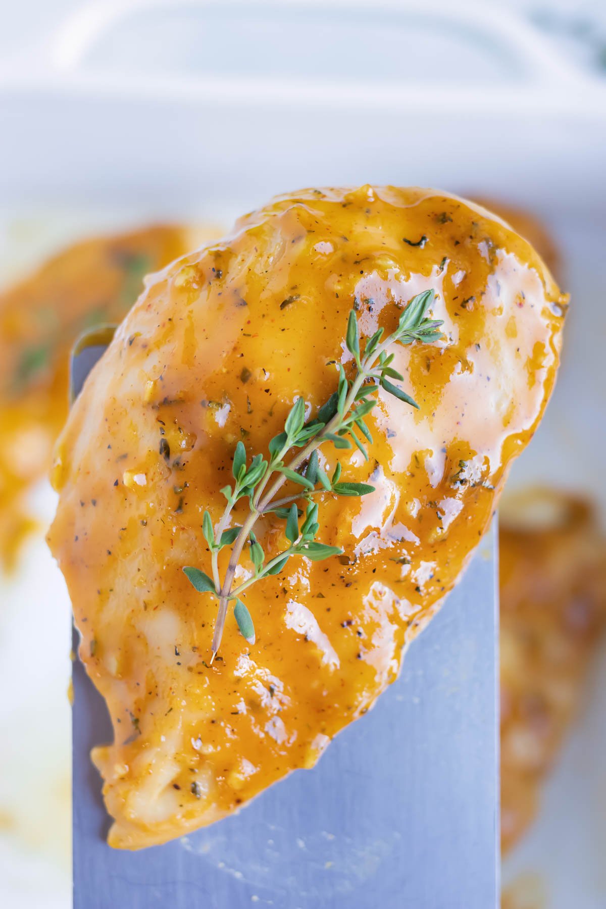 A spatula picking up a piece of chicken from a baking dish with a sprig of thyme on top.