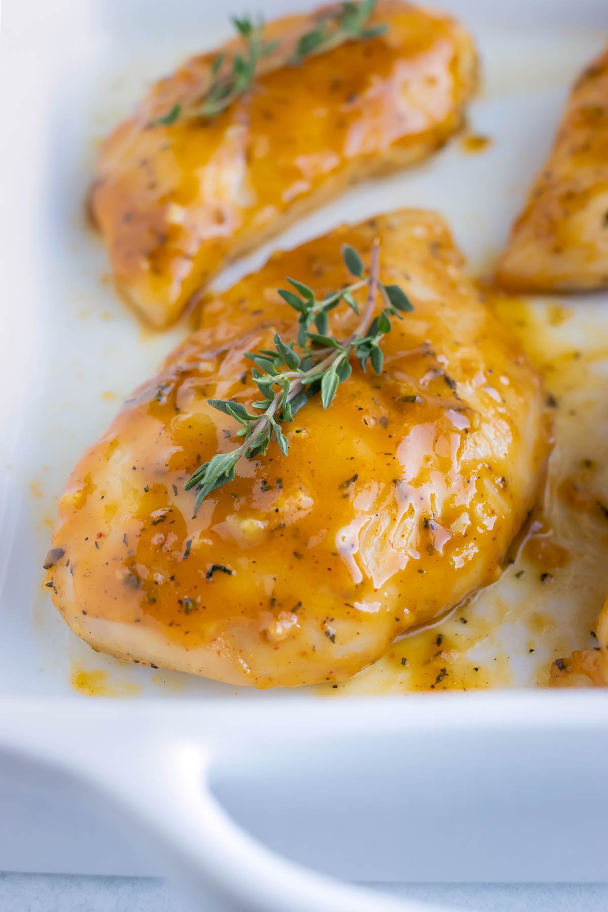 A white casserole dish with chicken breasts that have been baked in the oven and are covered in a honey-colored sauce.