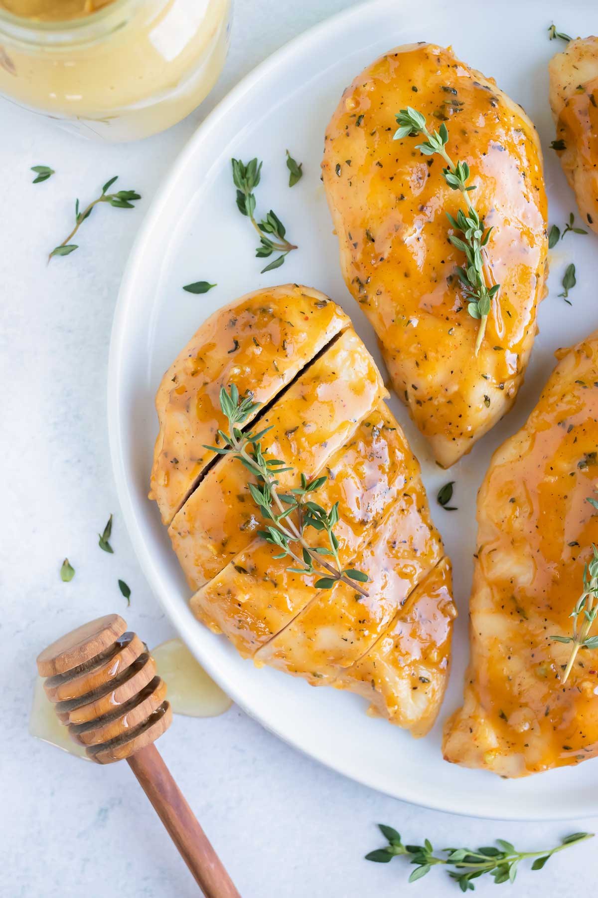 Honey mustard glazed chicken with thyme sprigs on top and next to a jar full of Dijon mustard.