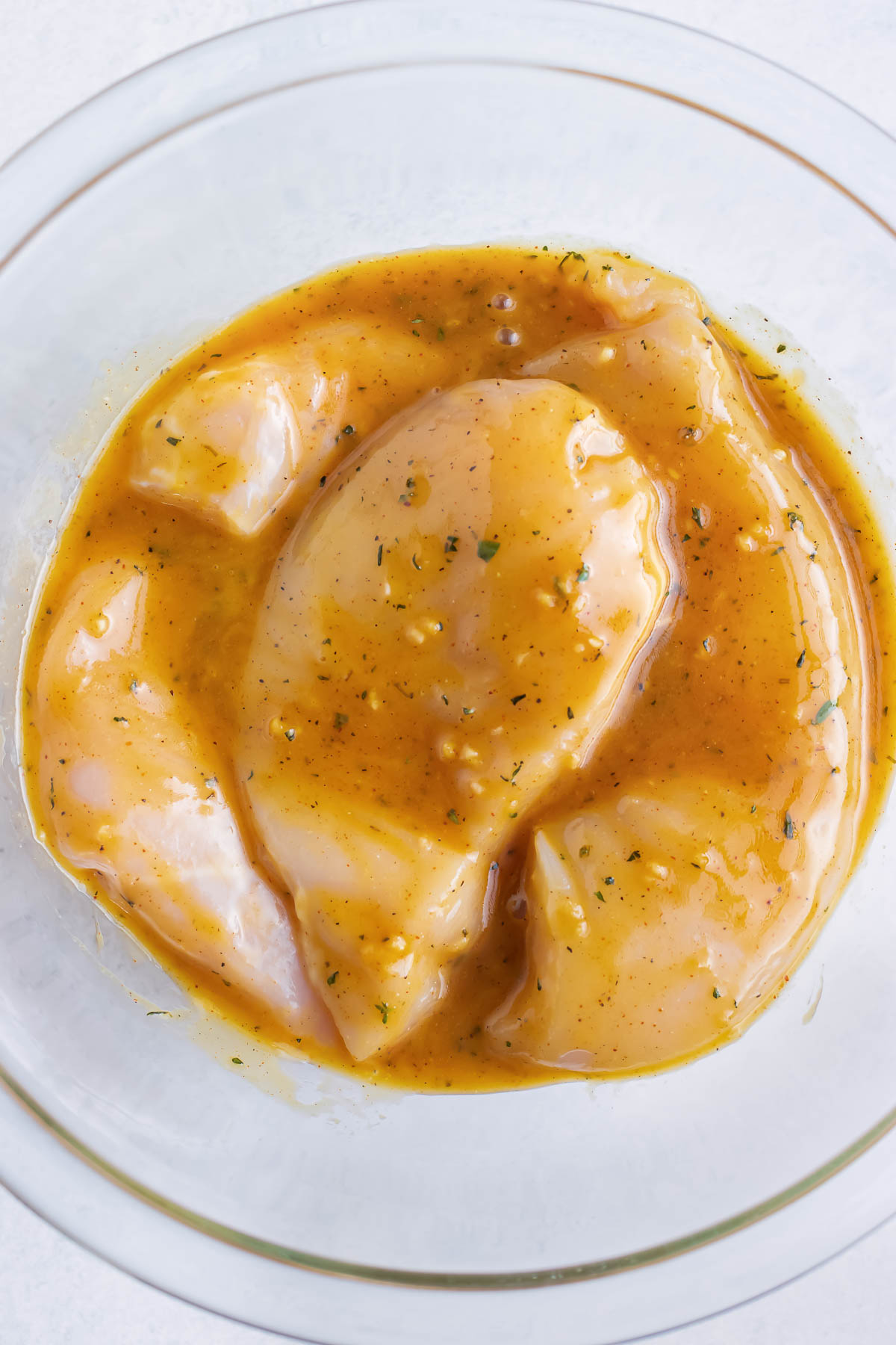 A clear glass bowl full of chicken covered in a honey mustard marinade.