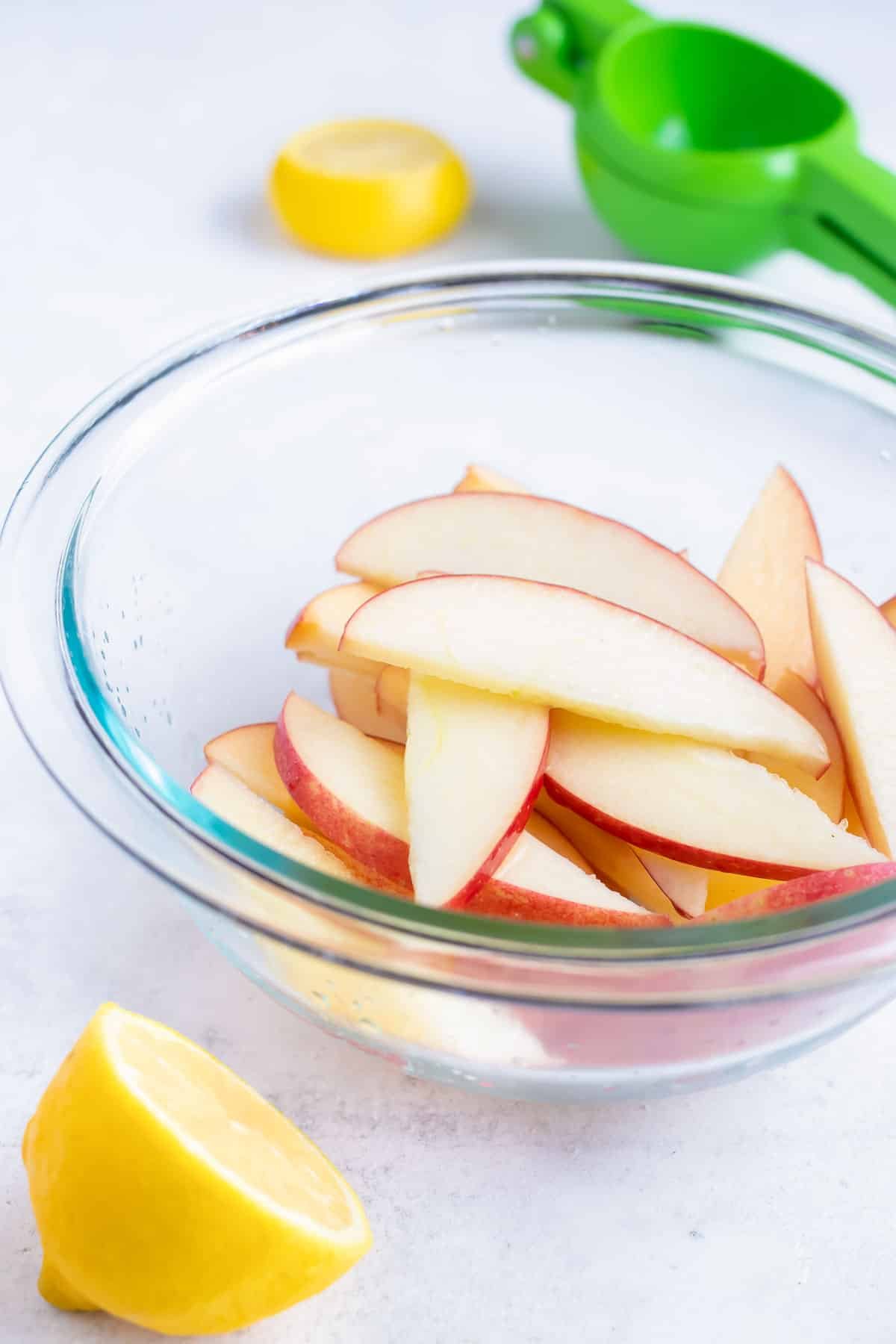 Fresh apple slices are placed in a bowl and tossed in lemon juice.