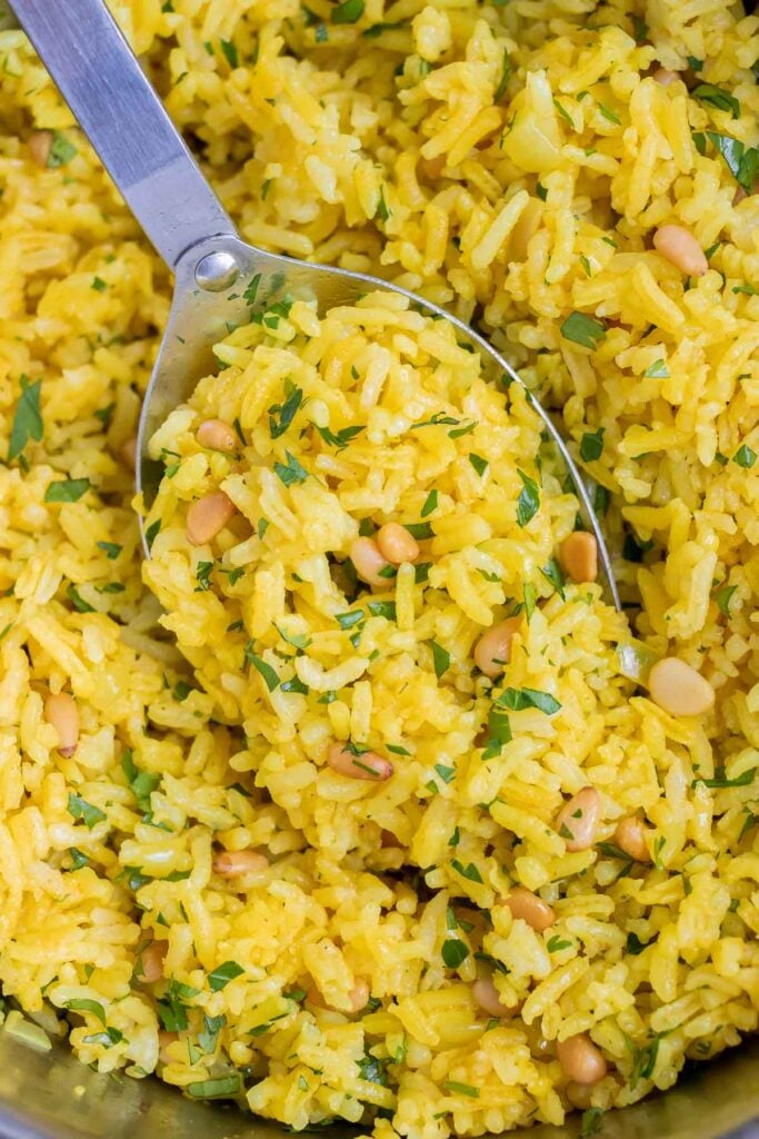 Greek yellow rice is served with a metal spoon from a metal pot.