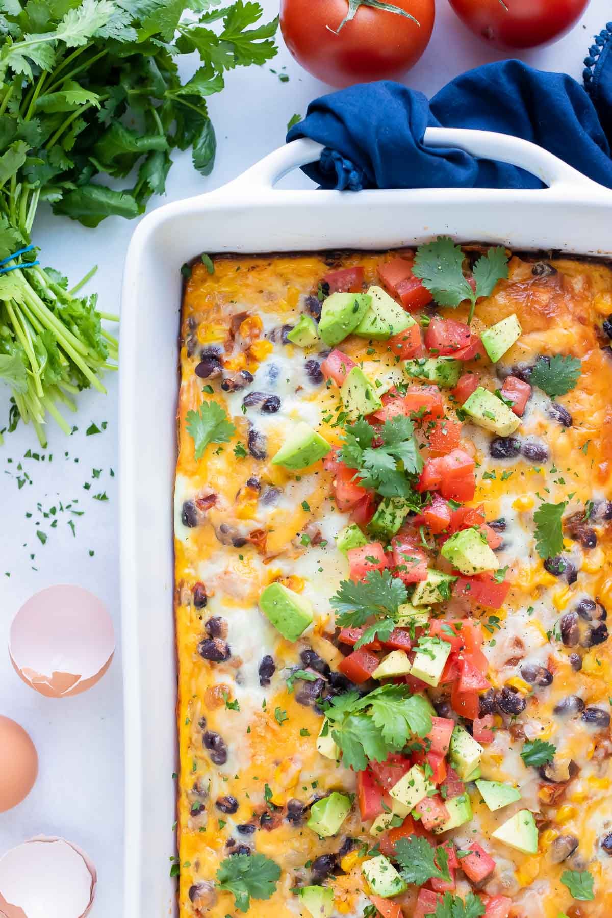 This Mexican Breakfast Casserole is served with fresh avocado and tomato for a healthy brunch.