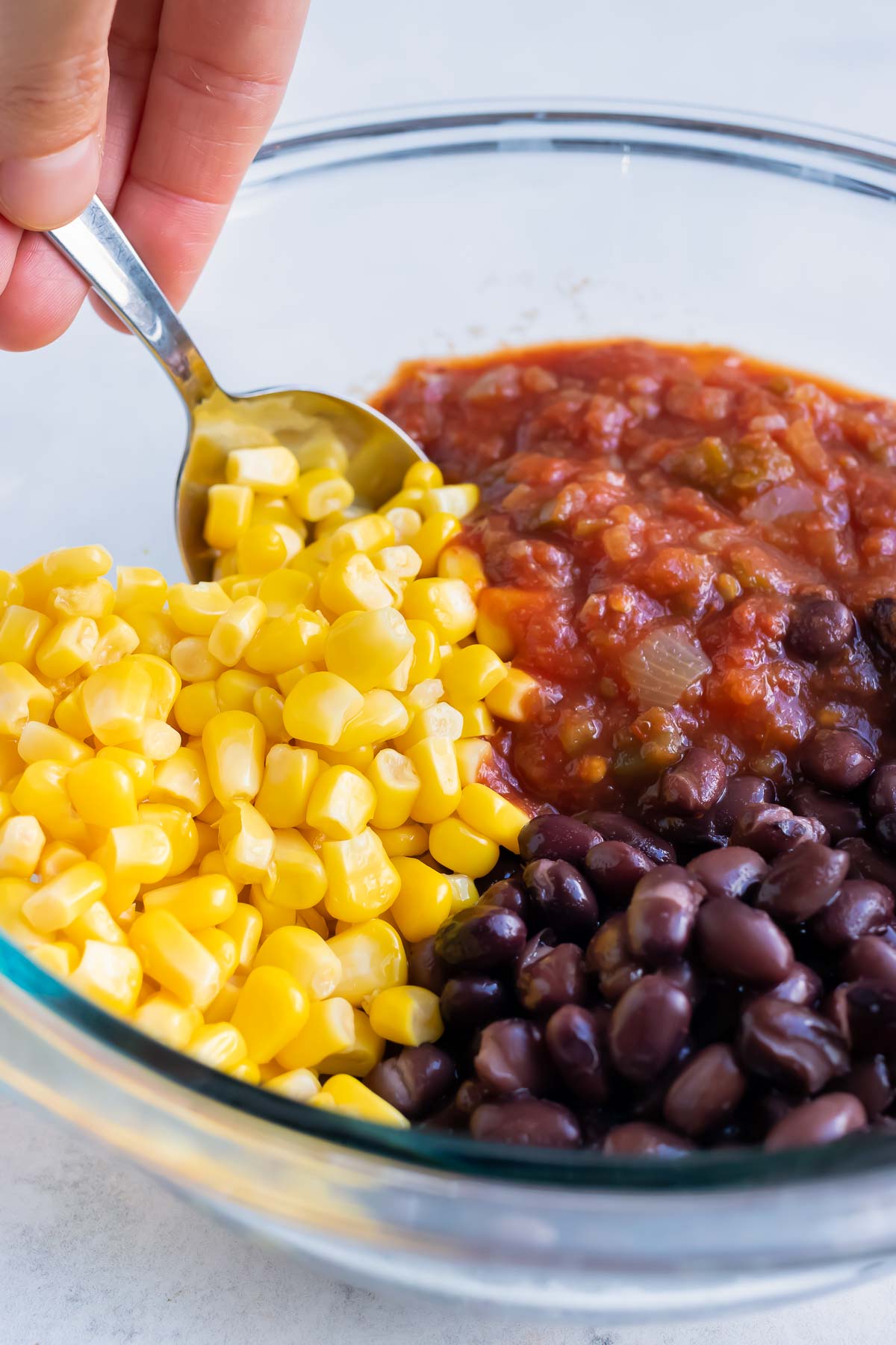 Canned corn, beans, and salsa are mixed together in a bowl.
