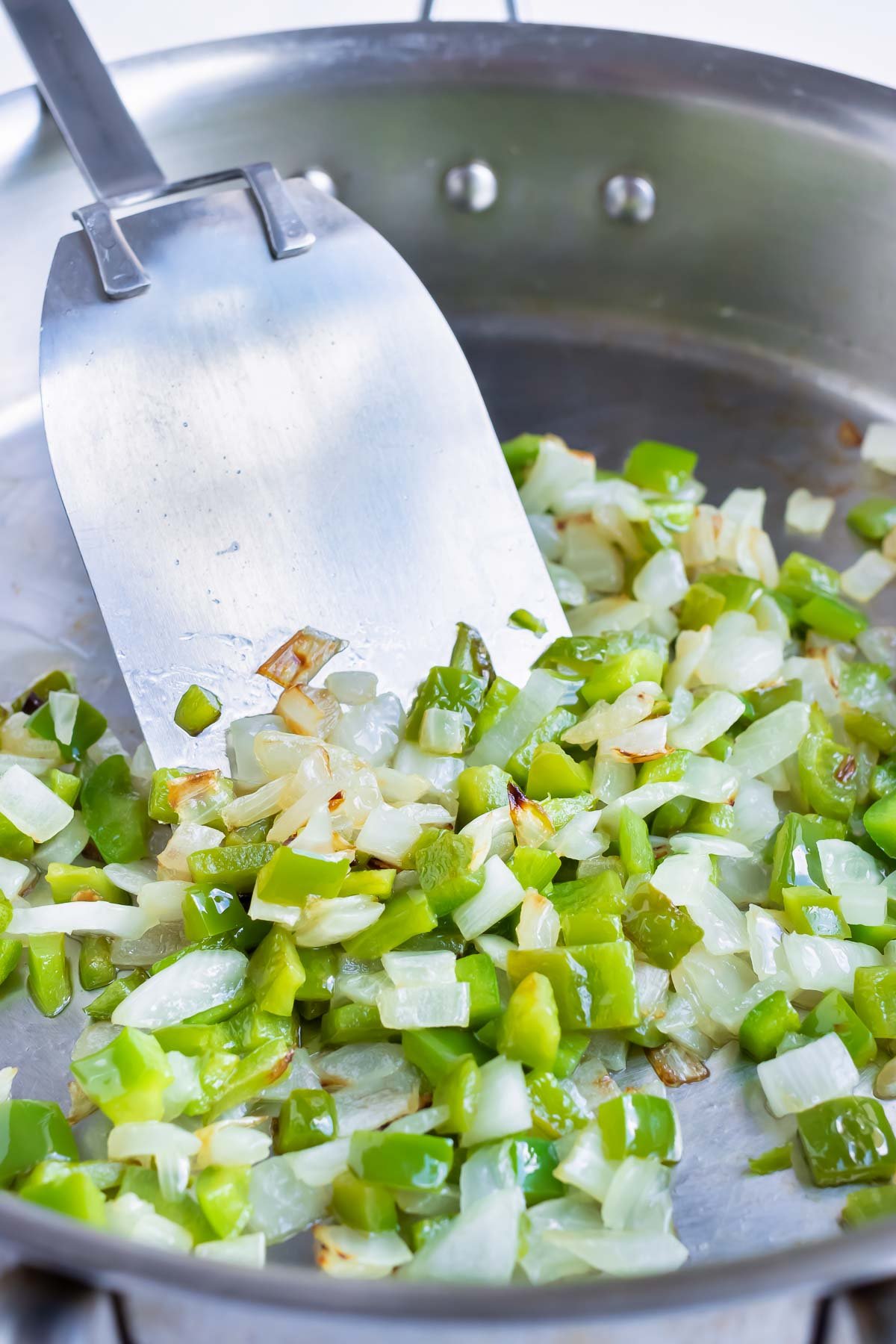 Onions and bell peppers are sautéed in a skillet.