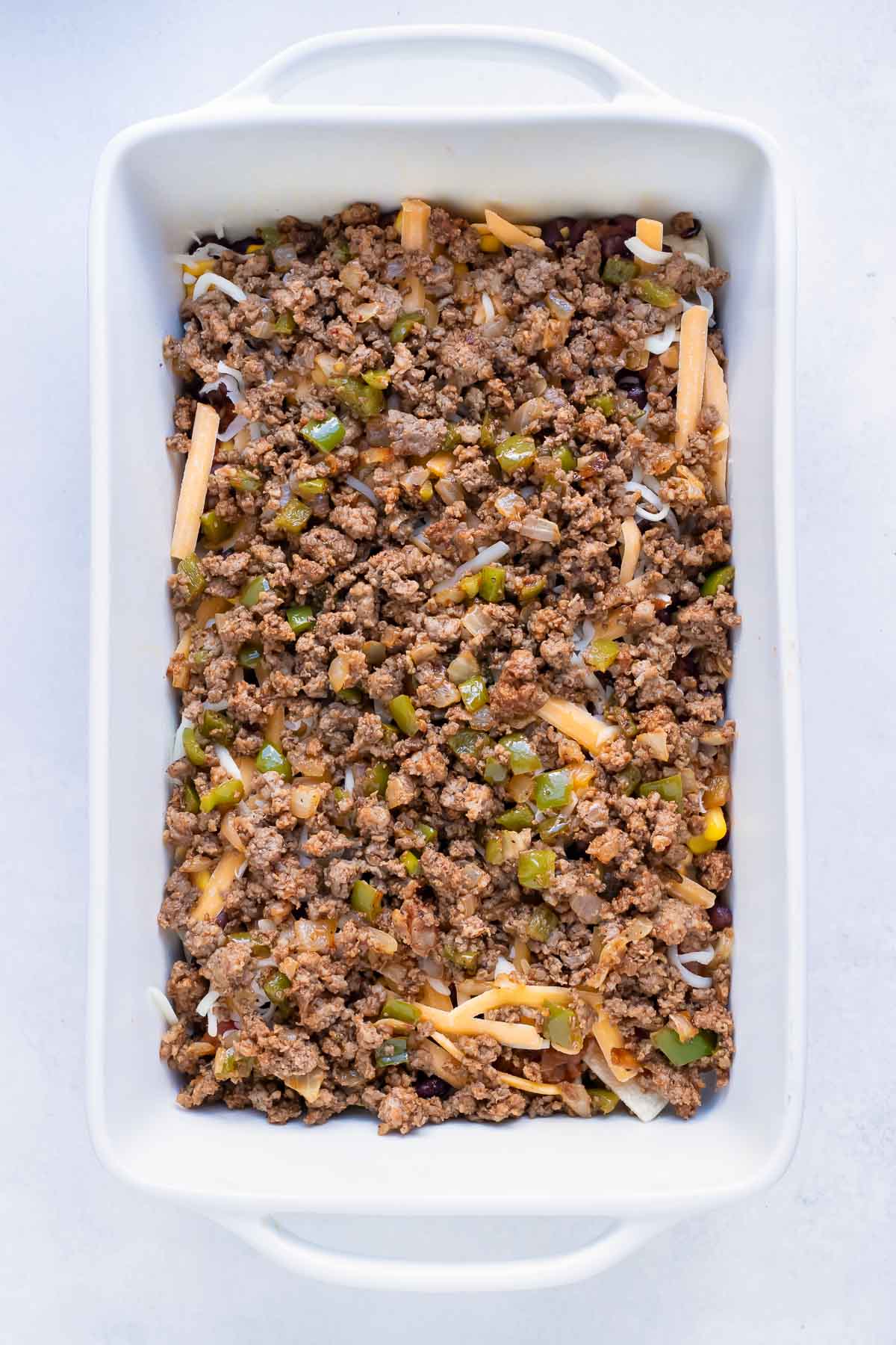 Ground meat and sautéed vegetables are placed in a casserole dish.