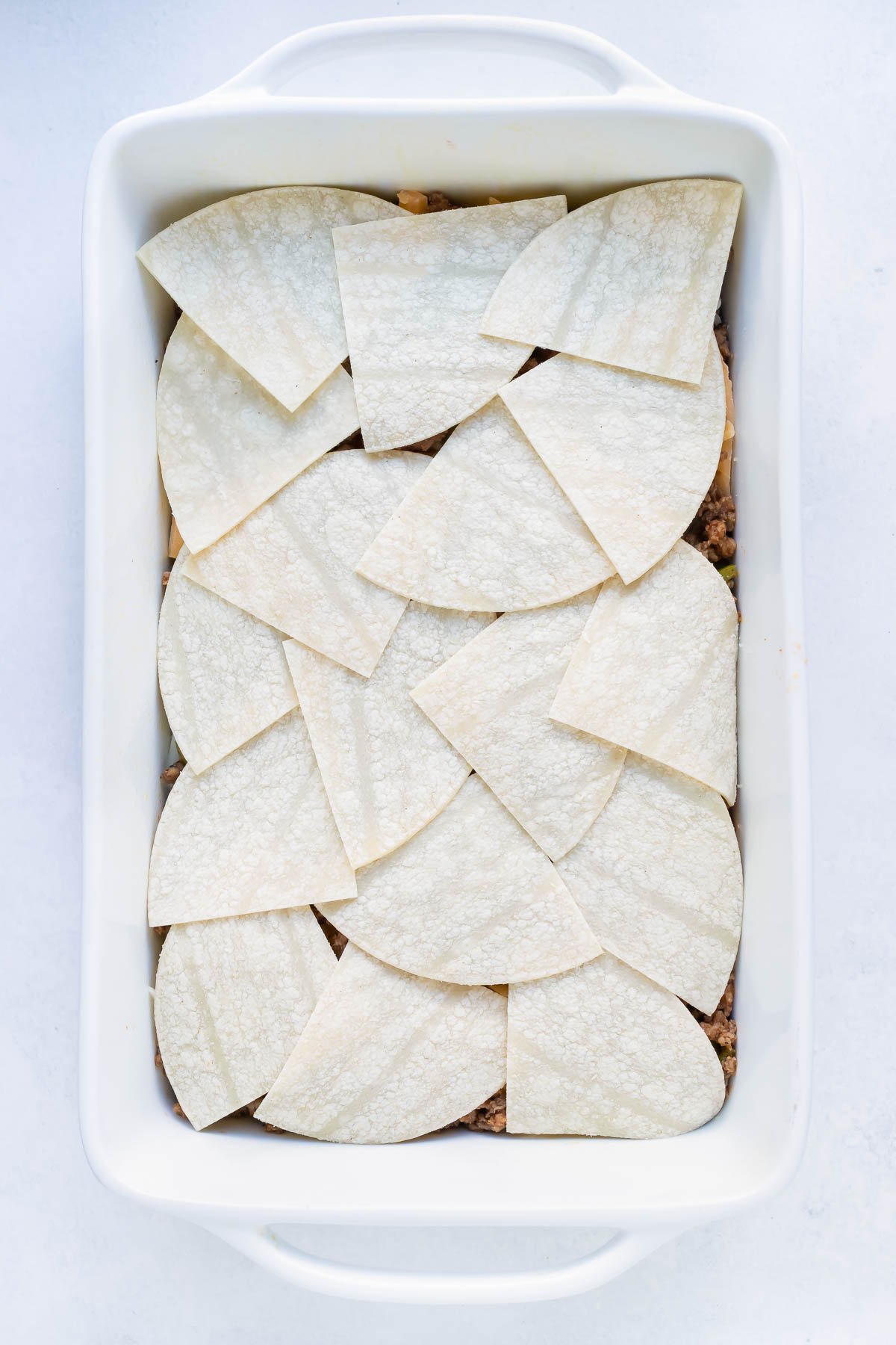 Chopped tortillas are layered on top of the cooked ground meat.