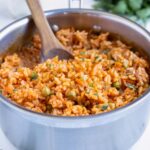 Homemade Mexican rice is dished with a wooden spoon from a pot.