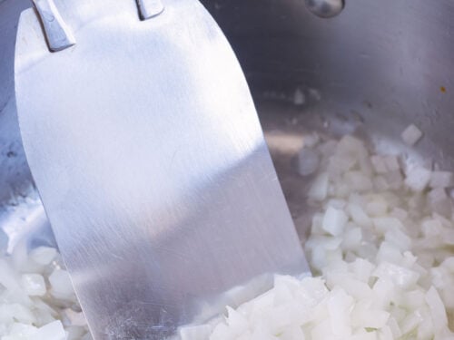 Diced onion is sautéed on the stove in a pot.
