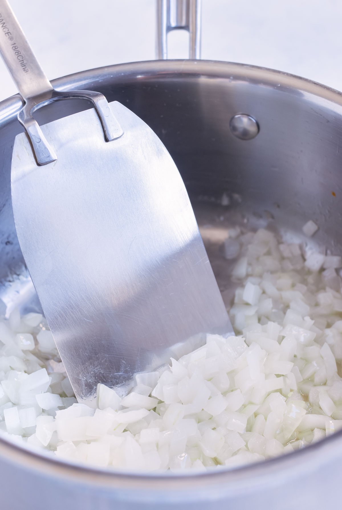 Diced onion is sautéed on the stove in a pot.