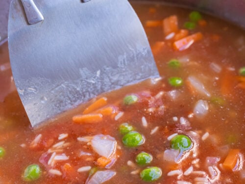 Broth, tomatoes, peas, carrots, and rice are added to the pot for a Mexican rice recipe.