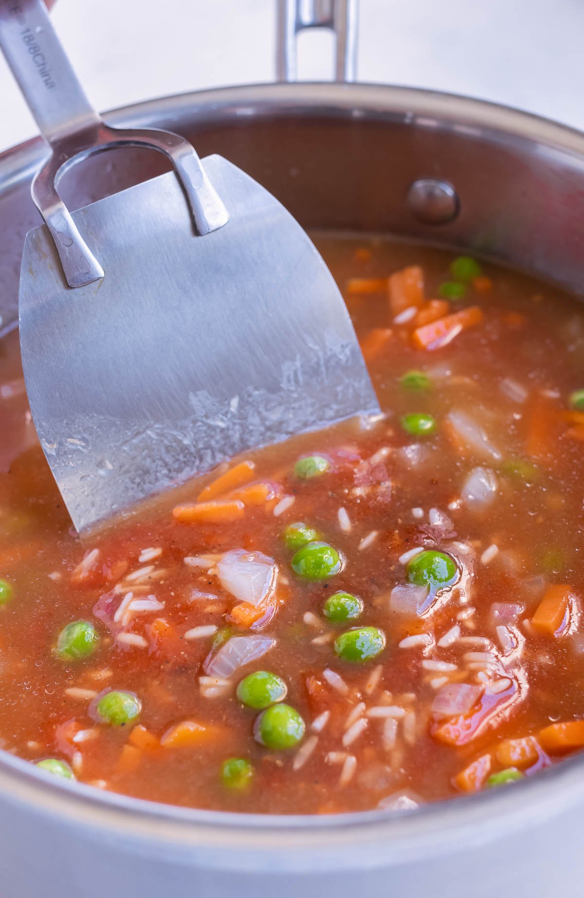 Broth, tomatoes, peas, carrots, and rice are added to the pot.